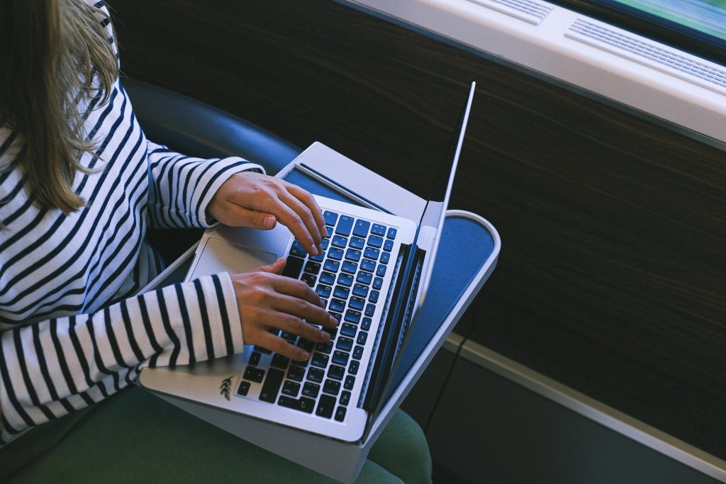 pexels-photo-12663328-12663328 A woman in a striped shirt types on a laptop while traveling on a train, showcasing remote work lifestyle.